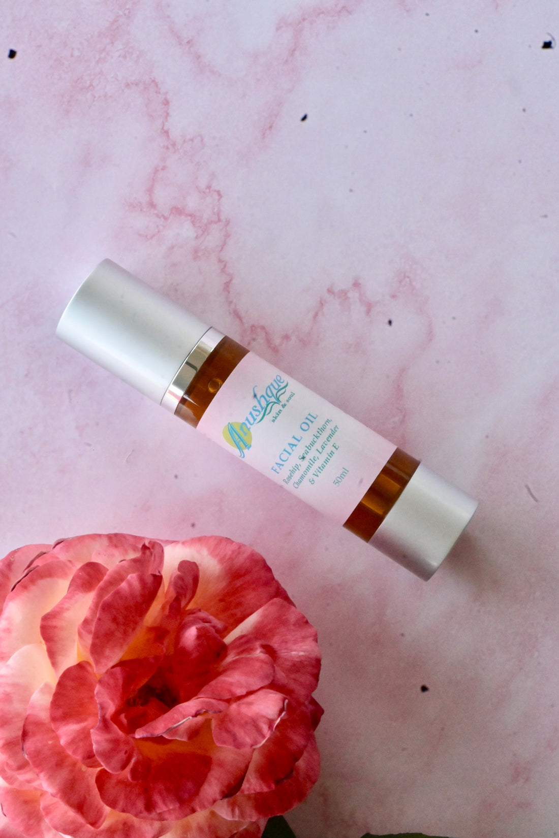 Pump bottle of face oil and a rose next to it.