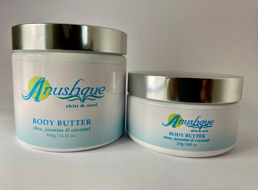 Two white tubs of body butter with shiny silver lids, containing shea butter, coconut, and jasmine extracts. Available in sizes 250g and 400g for luxurious skincare.